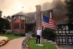 Seorang pria menurunkan bendera di luar rumah sepupunya yang terbakar di Kebakaran Eaton di Altadena California AS 8 Januari 2025. REUTERSDavid Swanson